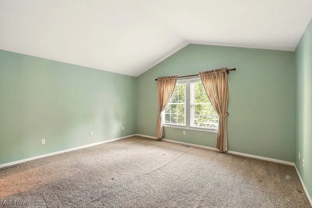 Carpeted spare room with lofted ceiling and baseboards