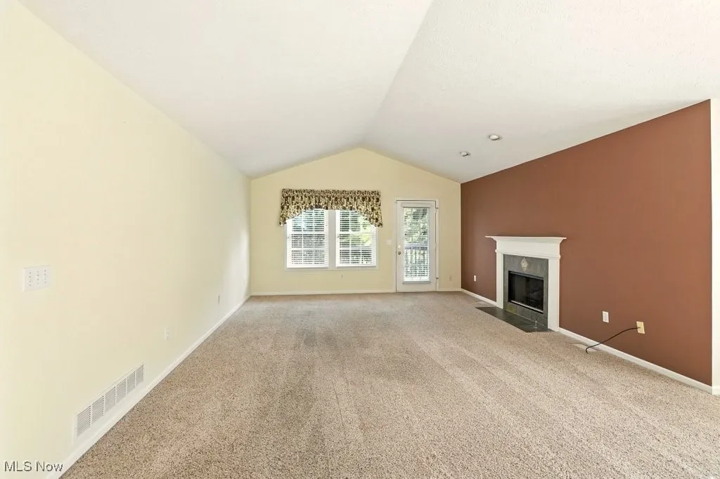Unfurnished living room featuring light colored carpet, a high end fireplace, and lofted ceiling