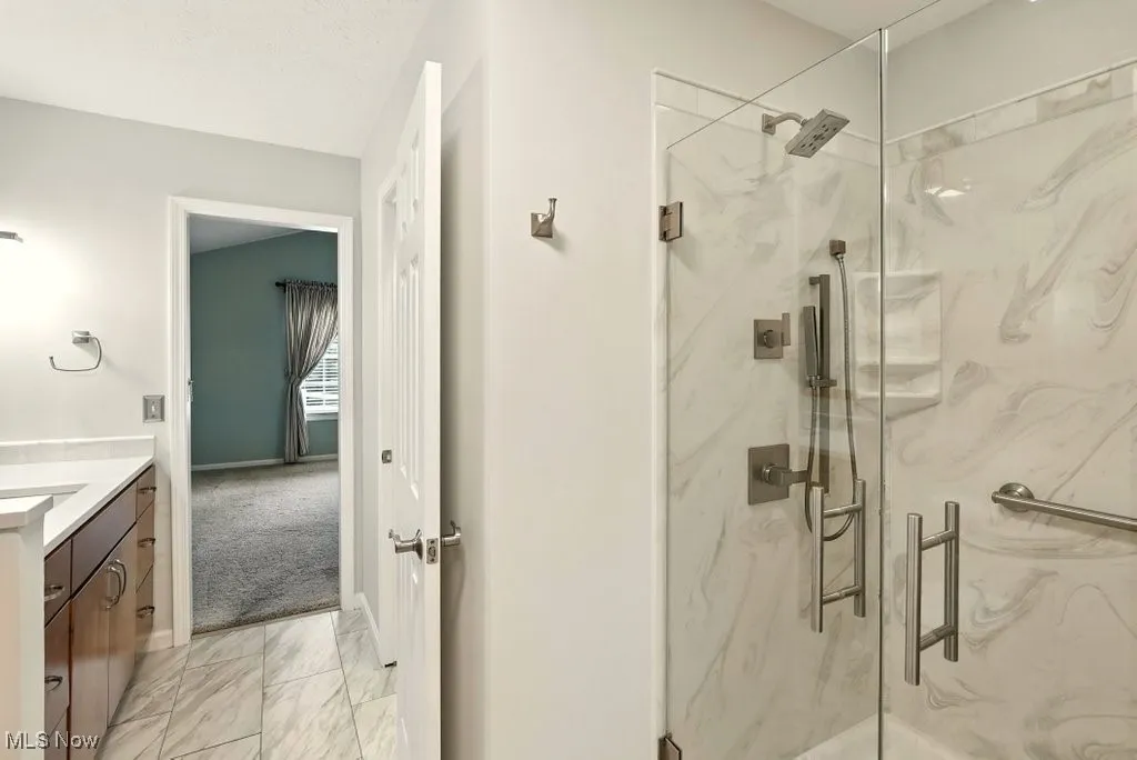 Bathroom featuring a marble finish shower, marble look tiles, and vanity