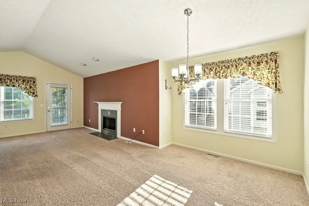 Unfurnished living room featuring a chandelier, carpet flooring, vaulted ceiling, a fireplace with flush hearth, and a textured ceiling