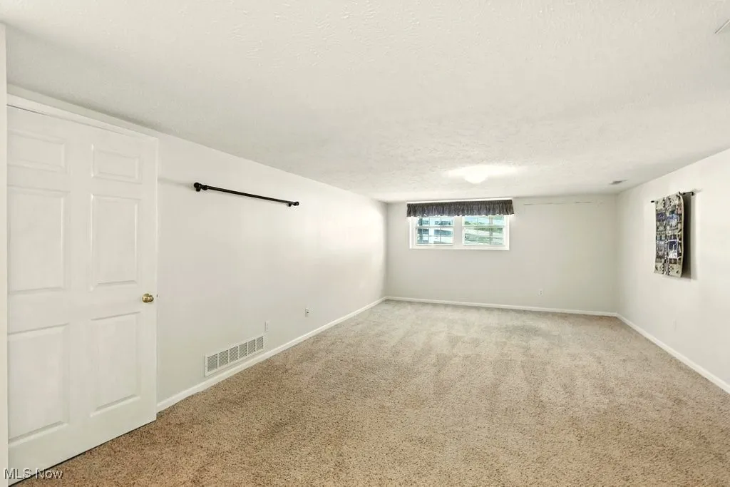 Carpeted spare room with a textured ceiling and baseboards