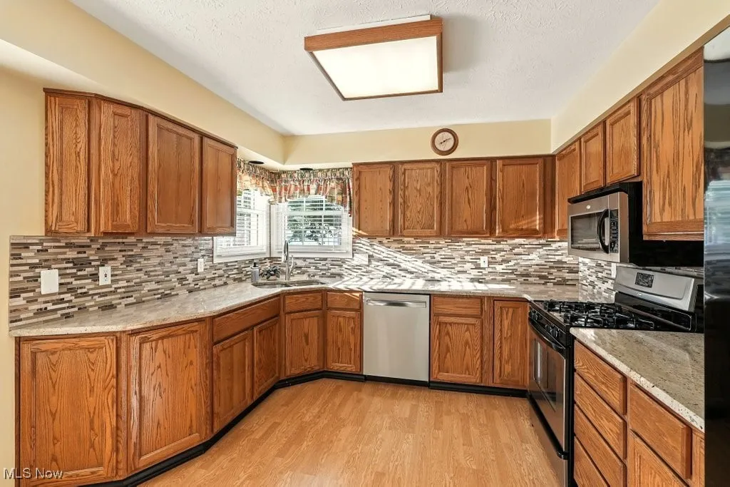 Kitchen with appliances with stainless steel finishes, decorative backsplash, brown cabinetry, and a textured ceiling