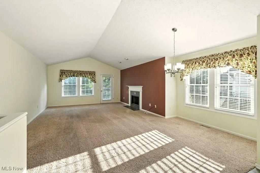 Unfurnished living room featuring carpet, a chandelier, lofted ceiling, and a fireplace with flush hearth