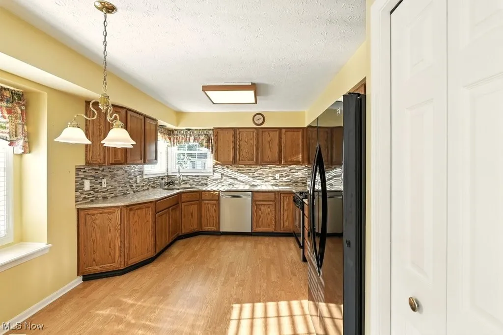 Kitchen featuring backsplash, brown cabinetry, freestanding refrigerator, light wood-style floors, and light countertops