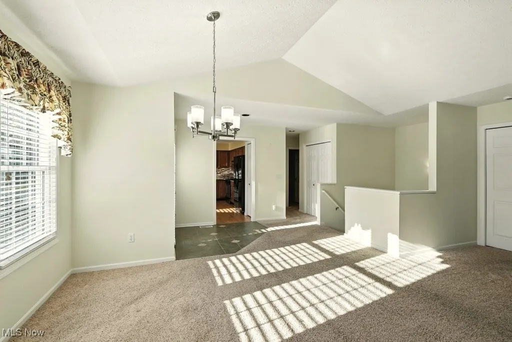 Carpeted empty room featuring a chandelier and vaulted ceiling