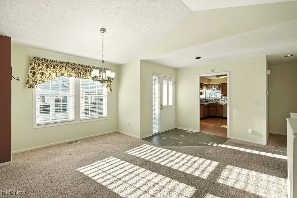 Unfurnished dining area featuring carpet, vaulted ceiling, a chandelier, and a textured ceiling