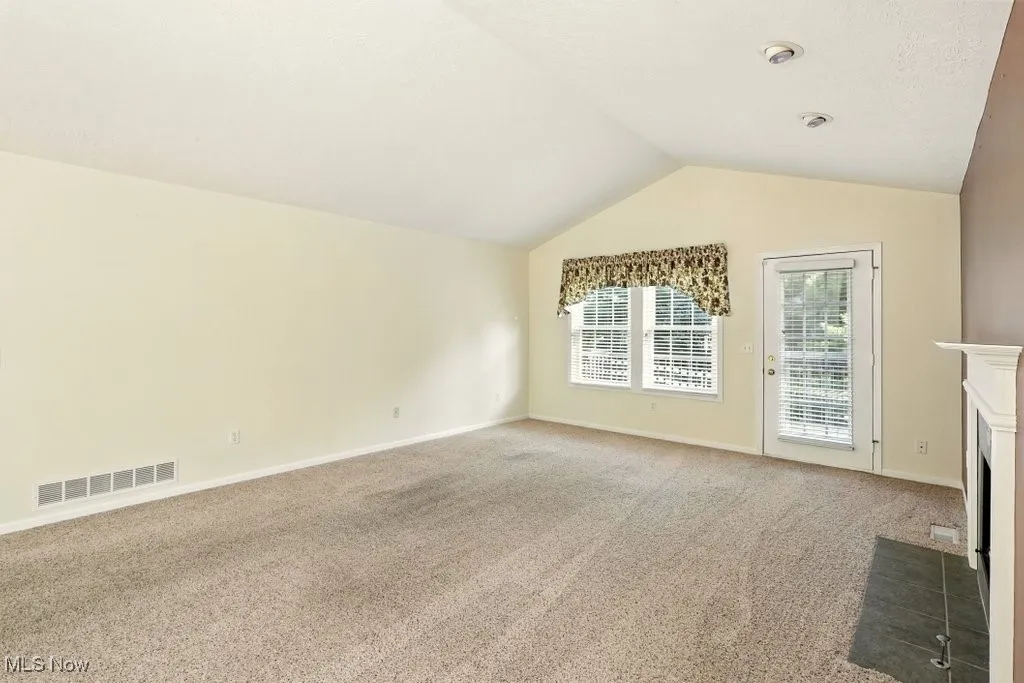 Unfurnished living room featuring carpet flooring, vaulted ceiling, and a fireplace with flush hearth