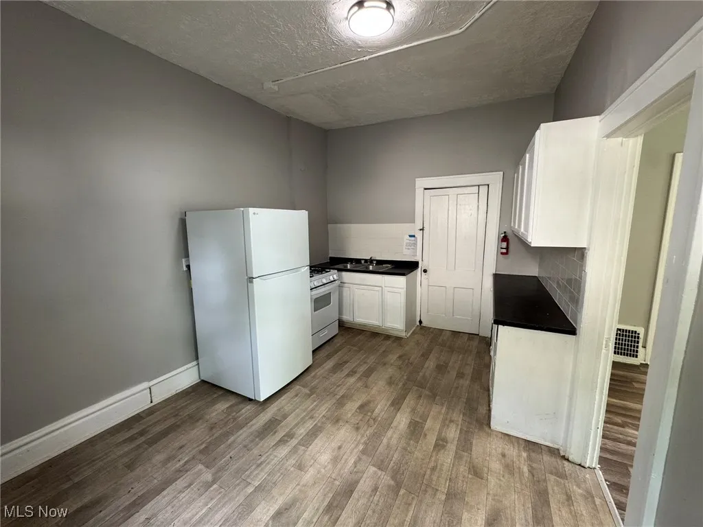 Kitchen featuring white appliances, dark countertops, dark wood-type LVP flooring, white cabinets, and a textured ceiling