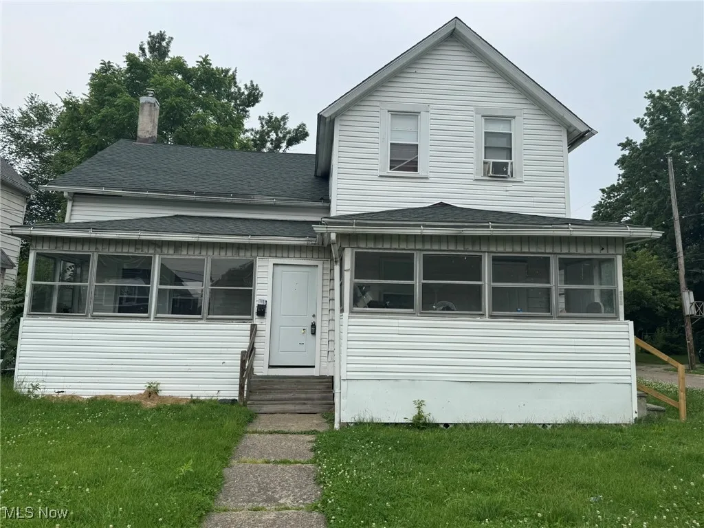 Traditional-style, side-by-side duplex home with a sunroom, entry steps, a shingled roof, and a front lawn