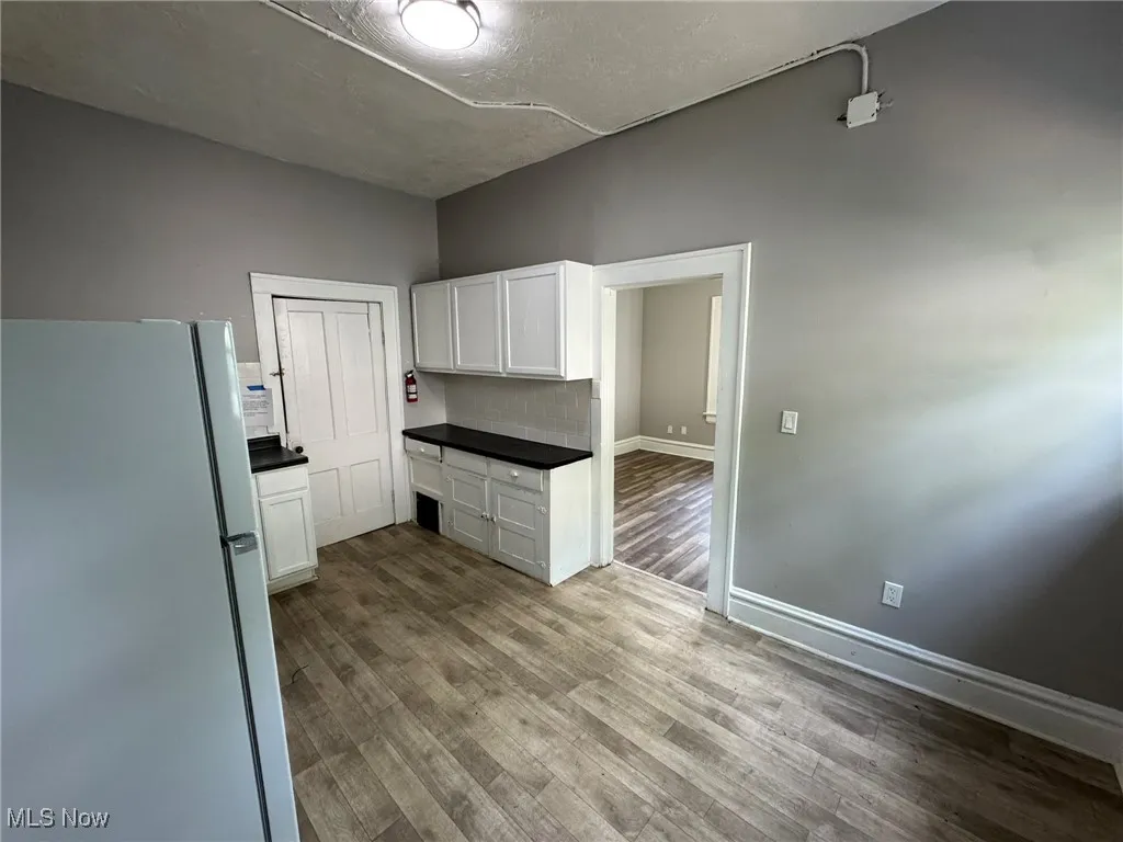 Kitchen featuring freestanding refrigerator, white cabinetry, dark countertops, and wood finished LVP floors