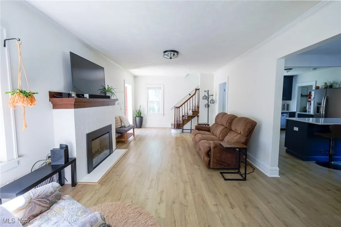 Living room with light wood finished floors, a fireplace, ornamental molding, and stairs