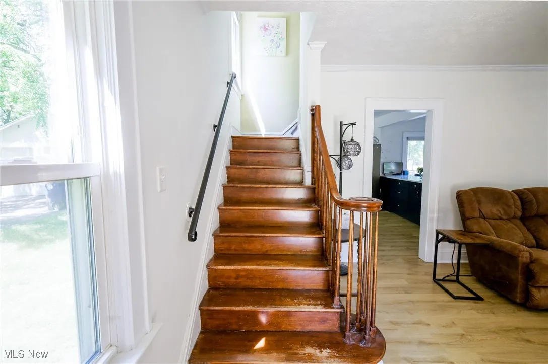Stairs featuring wood finished floors and crown molding