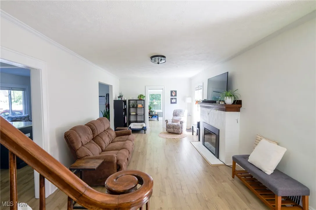 Living area with plenty of natural light, light wood-type flooring, a glass covered fireplace, and crown molding