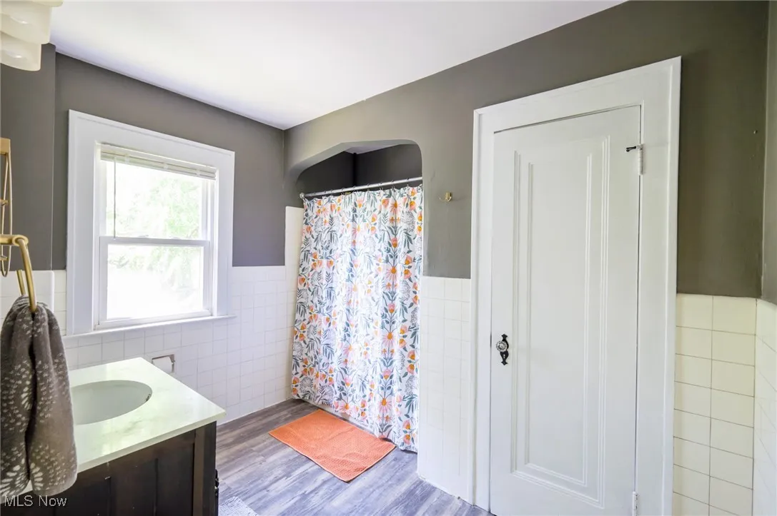 Full bath featuring wainscoting, wood finished floors, tile walls, vanity, and a shower with shower curtain