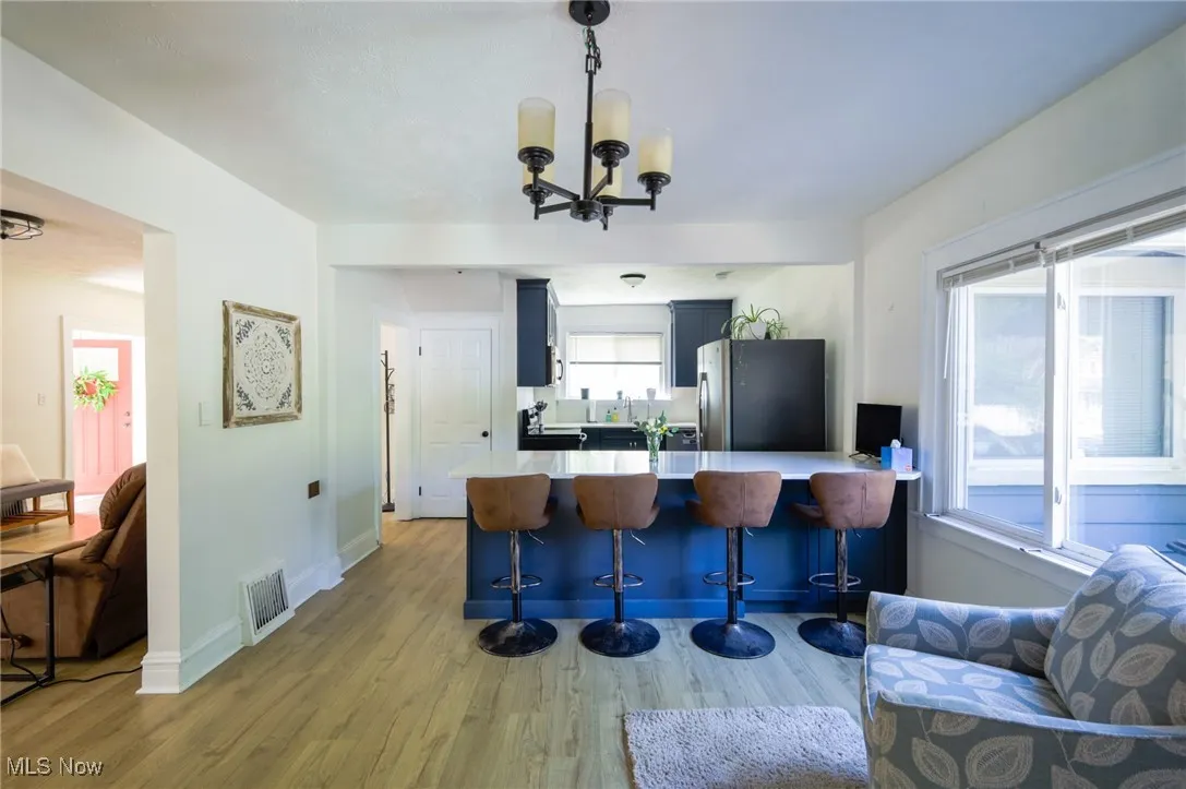 Kitchen featuring stainless steel fridge with ice dispenser, a peninsula, light wood finished floors, a kitchen bar, and a chandelier