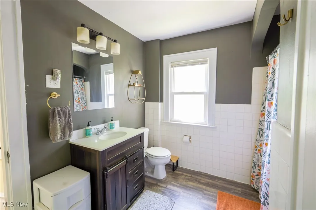 Full bathroom with wood finished floors, tile walls, plenty of natural light, vanity, and wainscoting