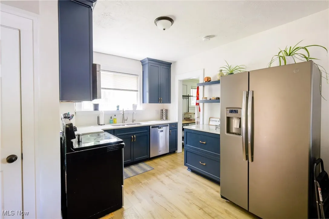 Kitchen featuring blue cabinetry, appliances with stainless steel finishes, light countertops, light wood-type flooring, and open shelves