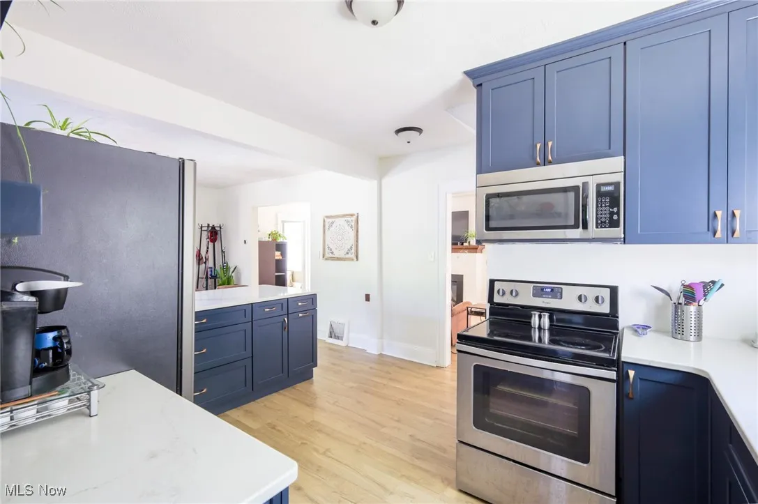 Kitchen with appliances with stainless steel finishes, blue cabinetry, and light wood-style floors