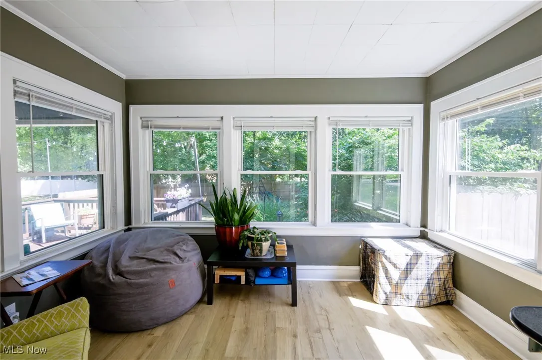 Sunroom / solarium featuring wood finished floors, ornamental molding, and plenty of natural light