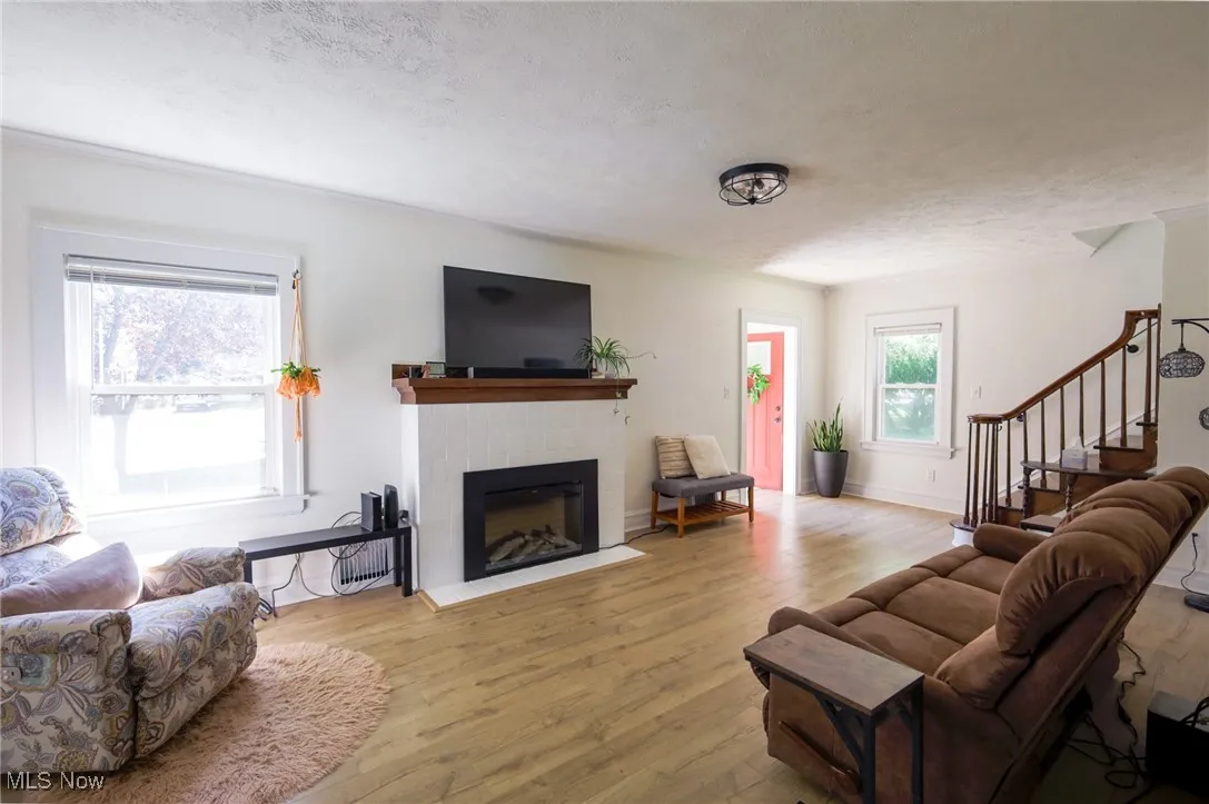 Living area with wood finished floors, a fireplace with flush hearth, a textured ceiling, and stairway