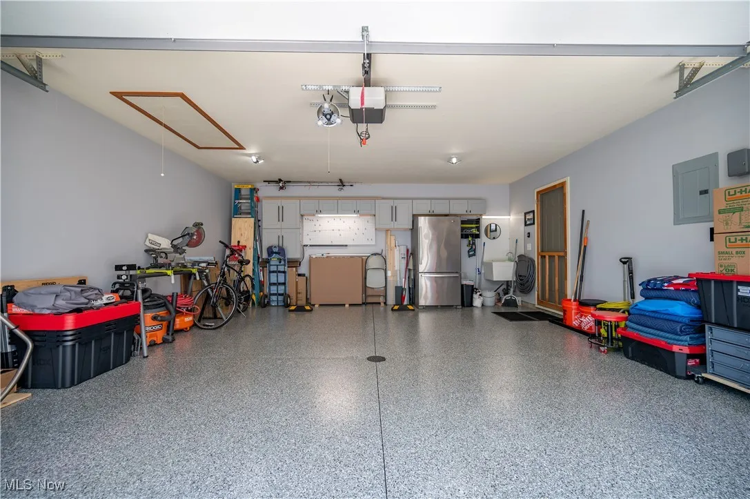 Garage featuring freestanding refrigerator, electric panel, and a garage door opener
