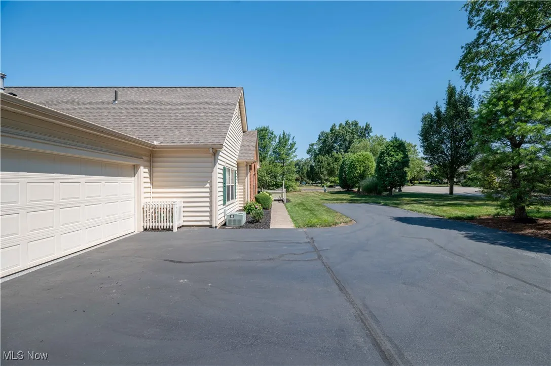 View of side of home with driveway, a shingled roof, and an attached garage