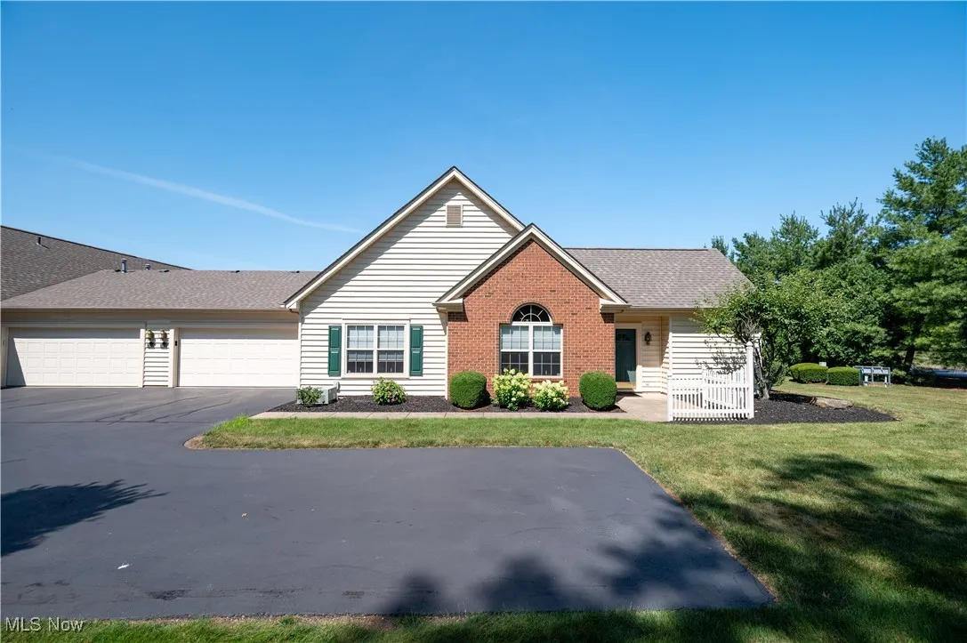 Ranch-style home featuring a front lawn, a shingled roof, a garage, brick siding, and driveway