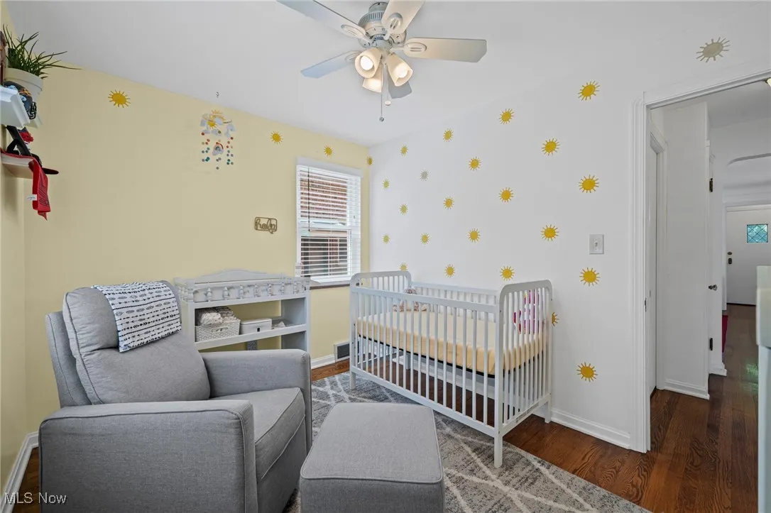 Bedroom featuring wood finished floors, a crib, and ceiling fan