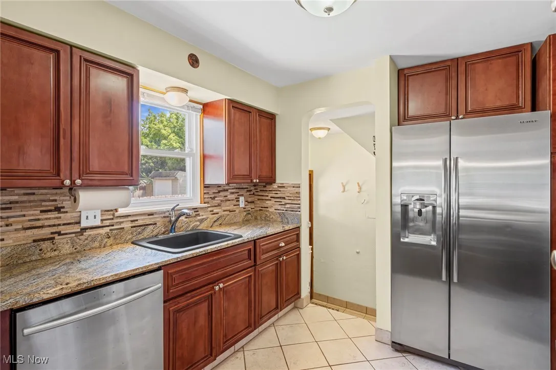 Kitchen with stainless steel appliances, decorative backsplash, light tile patterned flooring, and light stone countertops