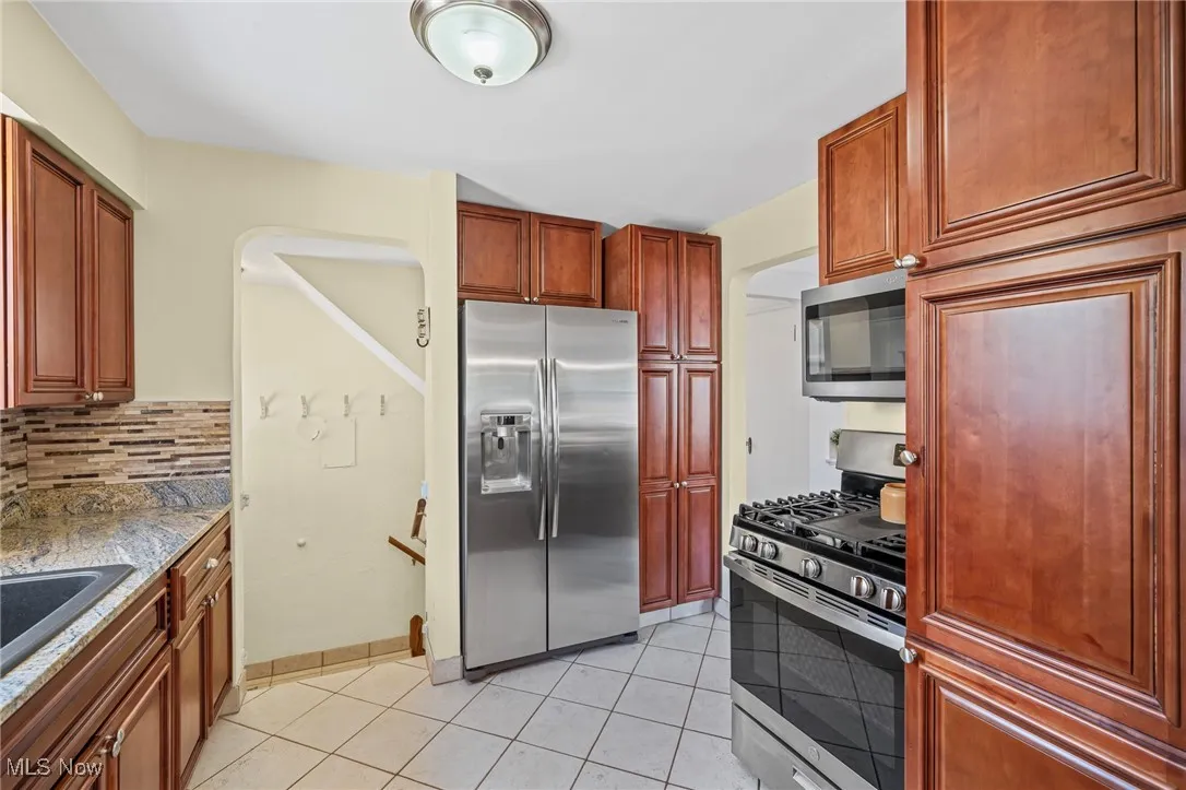 Kitchen featuring appliances with stainless steel finishes, light tile patterned floors, tasteful backsplash, arched walkways, and stone counters