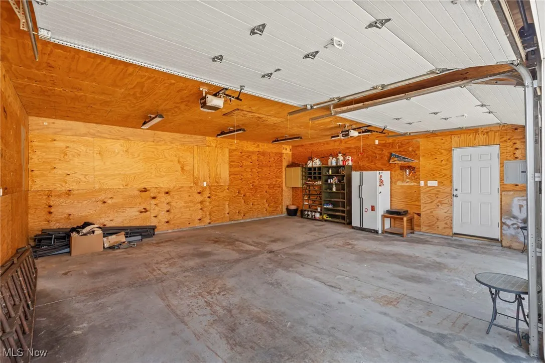 Garage with wooden walls, a workshop area, a garage door opener, and electric panel