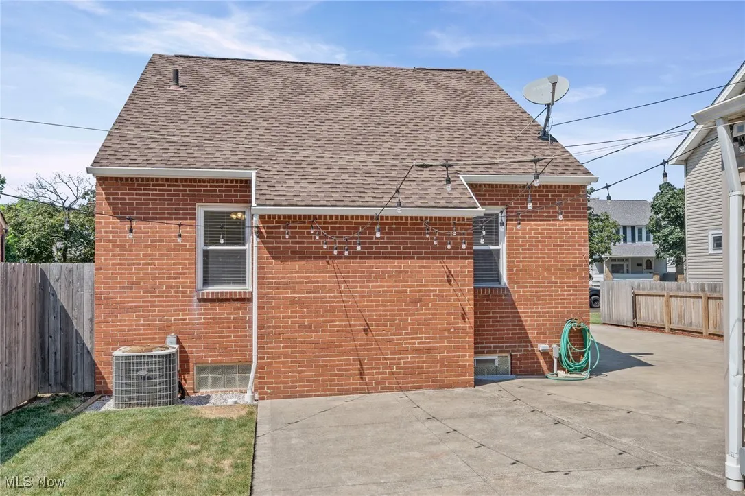 Back of house featuring brick siding, a patio area, roof with shingles, and a fenced backyard