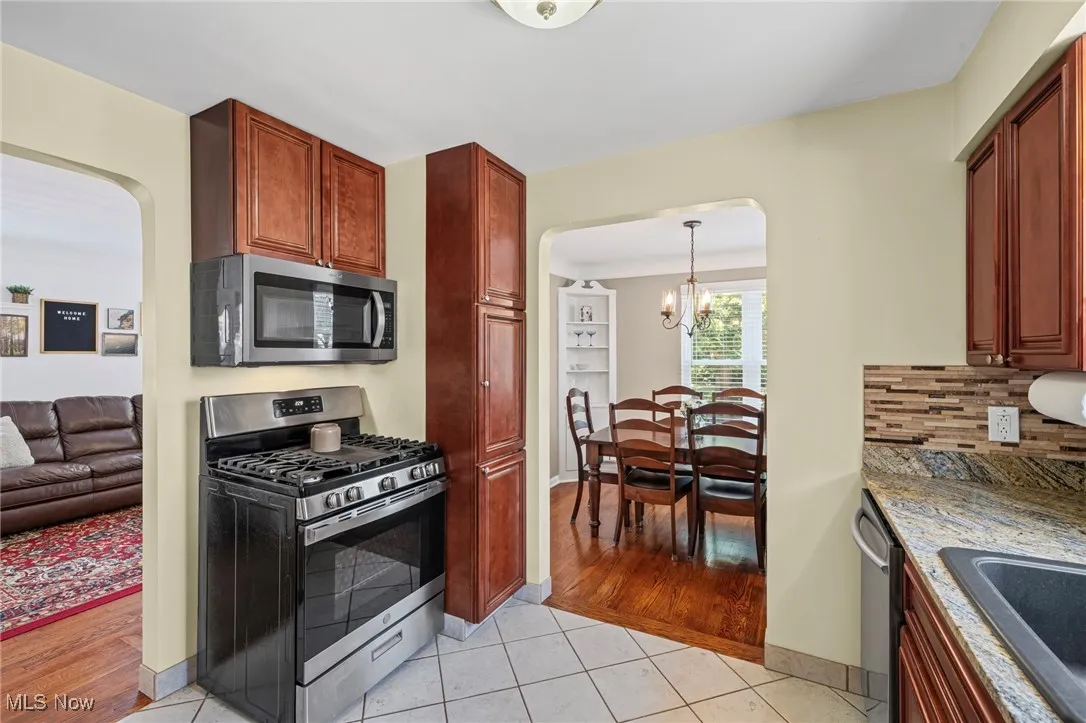 Kitchen featuring stainless steel appliances, arched walkways, a chandelier, light tile patterned flooring, and light stone counters