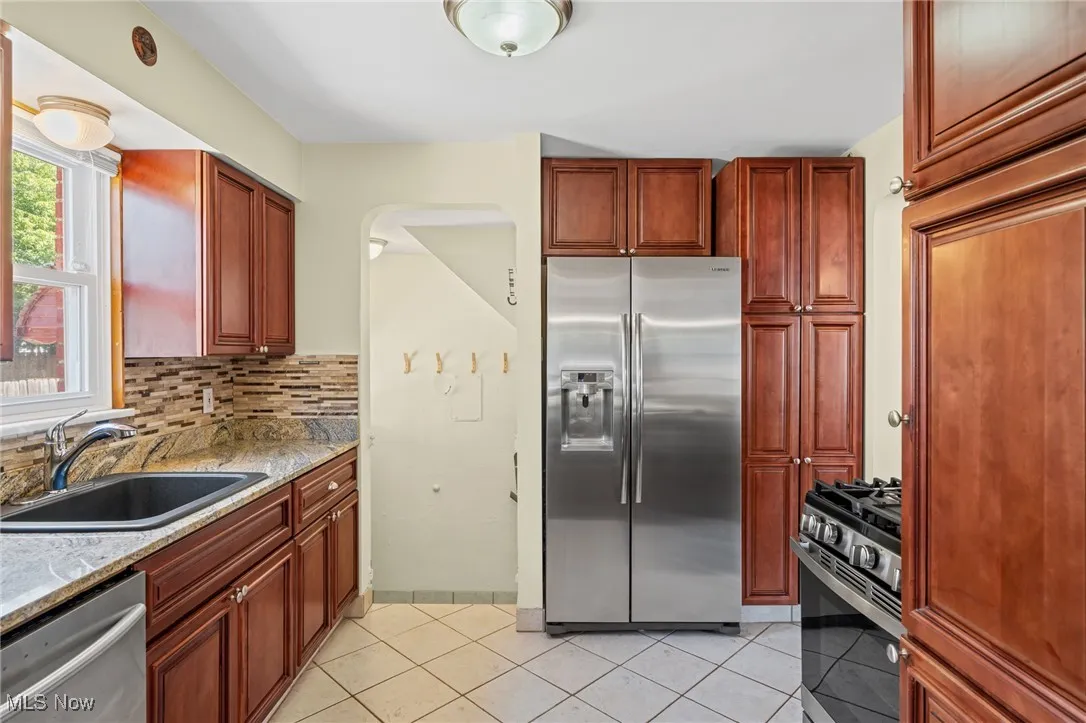 Kitchen featuring stainless steel appliances, tasteful backsplash, light tile patterned floors, light stone counters, and arched walkways