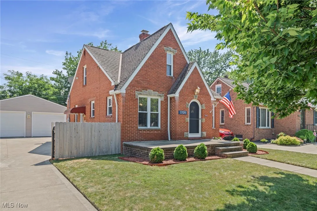 Tudor home featuring brick siding, an outbuilding, a garage, a chimney, and a shingled roof