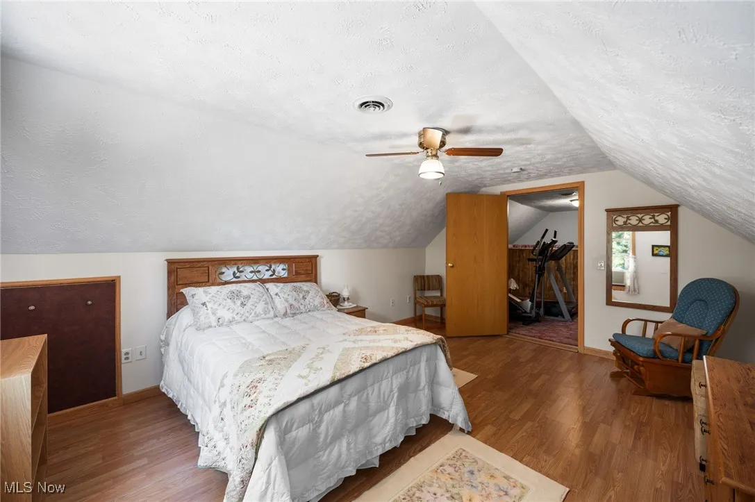 Bedroom with a textured ceiling, vaulted ceiling, wood finished floors, a walk in closet, and ceiling fan