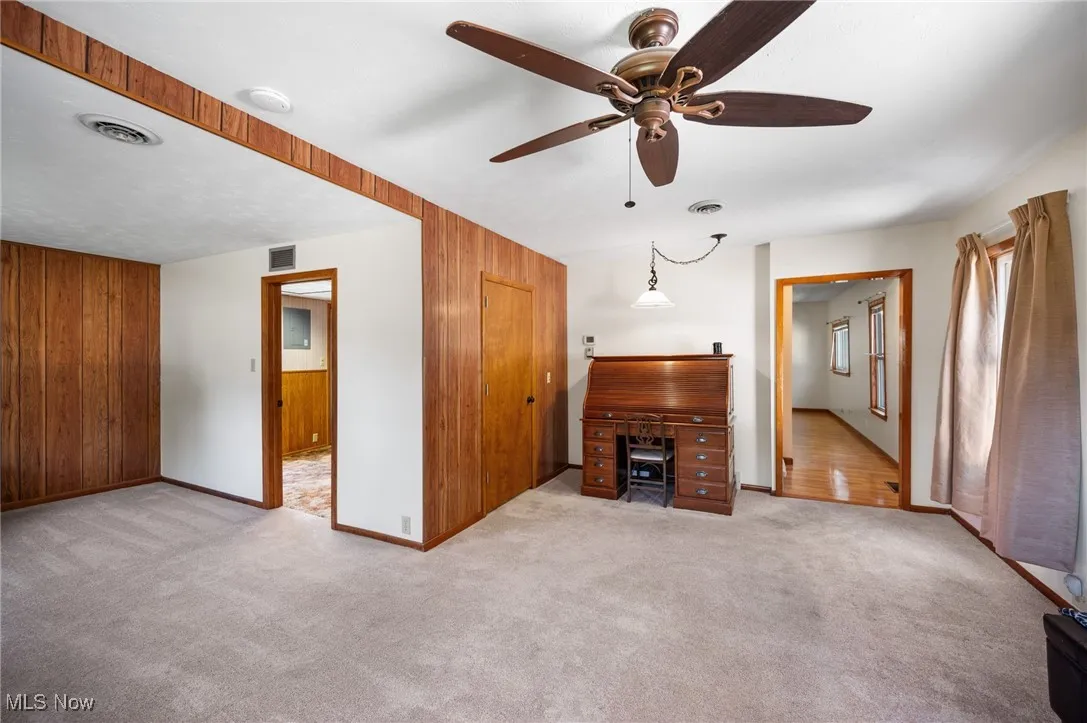 Unfurnished living room with carpet flooring, wood walls, and a ceiling fan