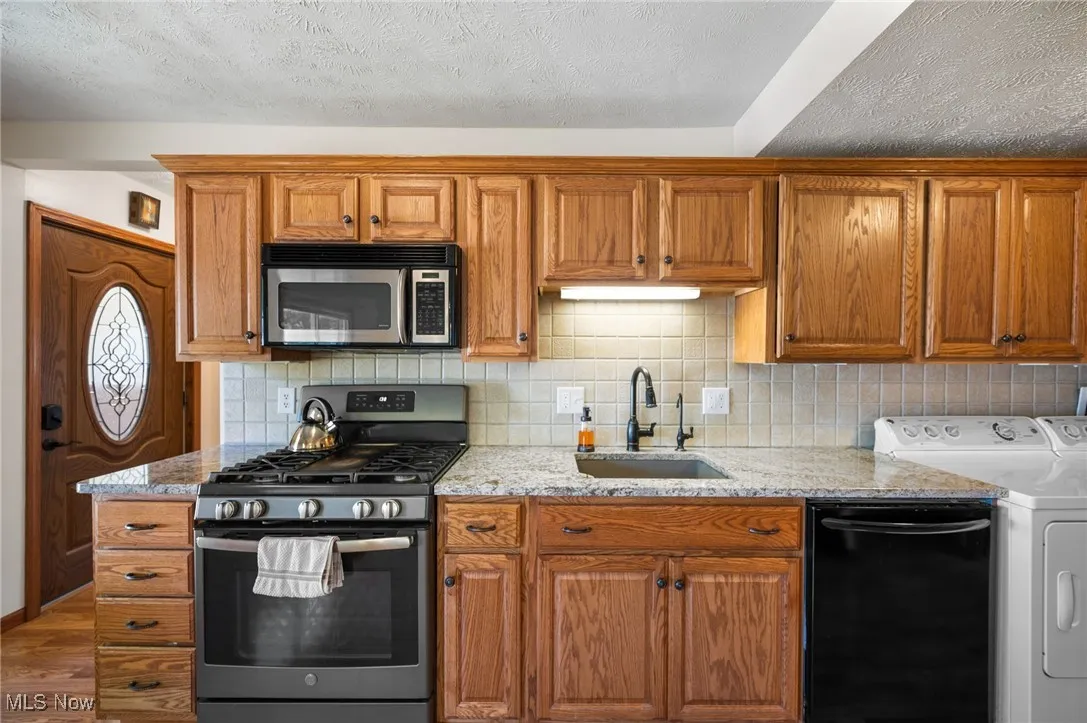 Kitchen featuring stainless steel appliances, backsplash, brown cabinets, and a textured ceiling