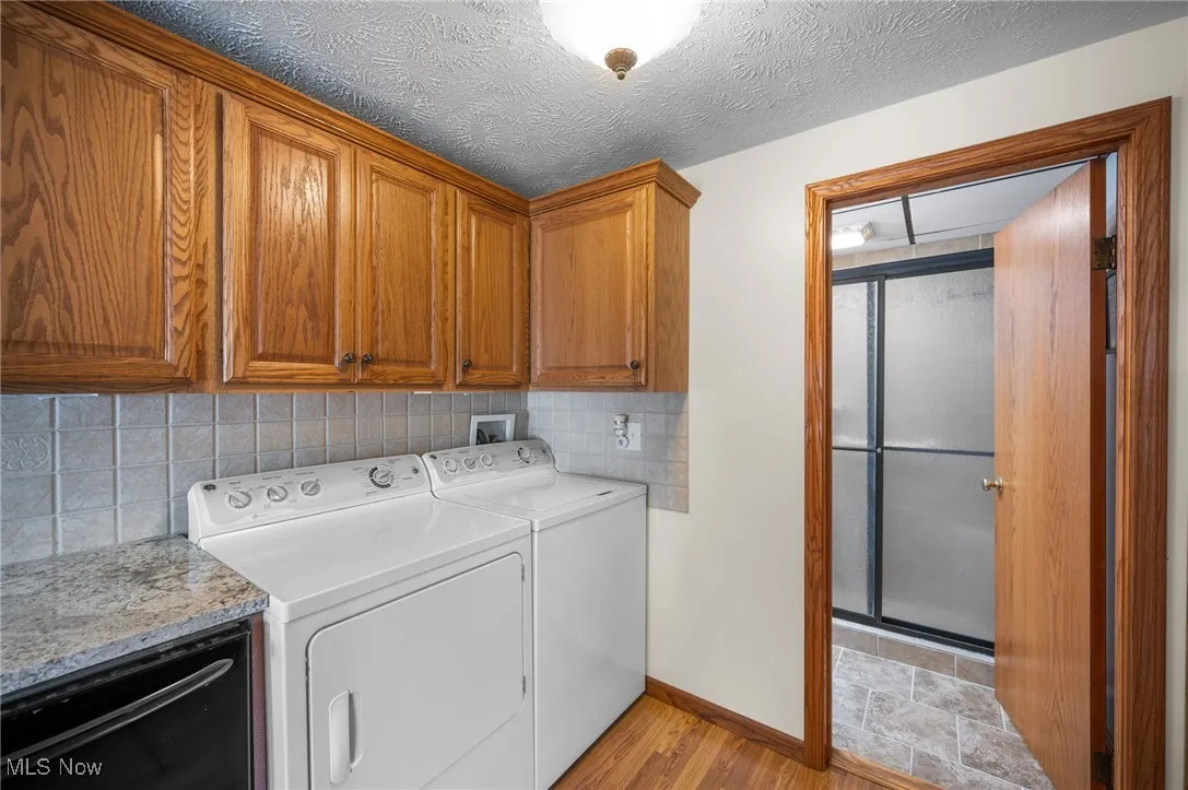 Laundry room featuring cabinet space, washer and clothes dryer, light wood finished floors, and a textured ceiling