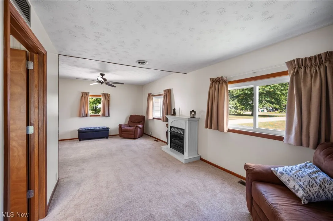 Living room featuring light carpet, a textured ceiling, a ceiling fan, and a glass covered fireplace