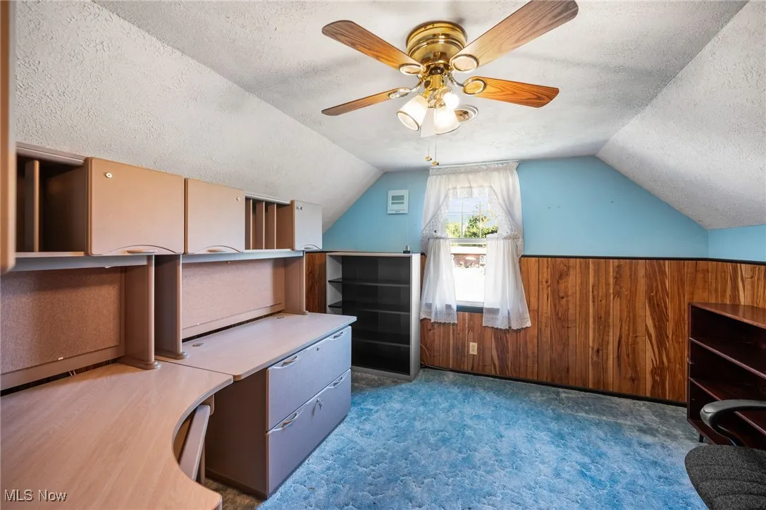 Additional living space with wooden walls, a textured ceiling, a wainscoted wall, vaulted ceiling, and ceiling fan