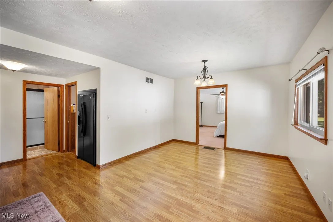 Empty room with light wood finished floors, a chandelier, and a textured ceiling
