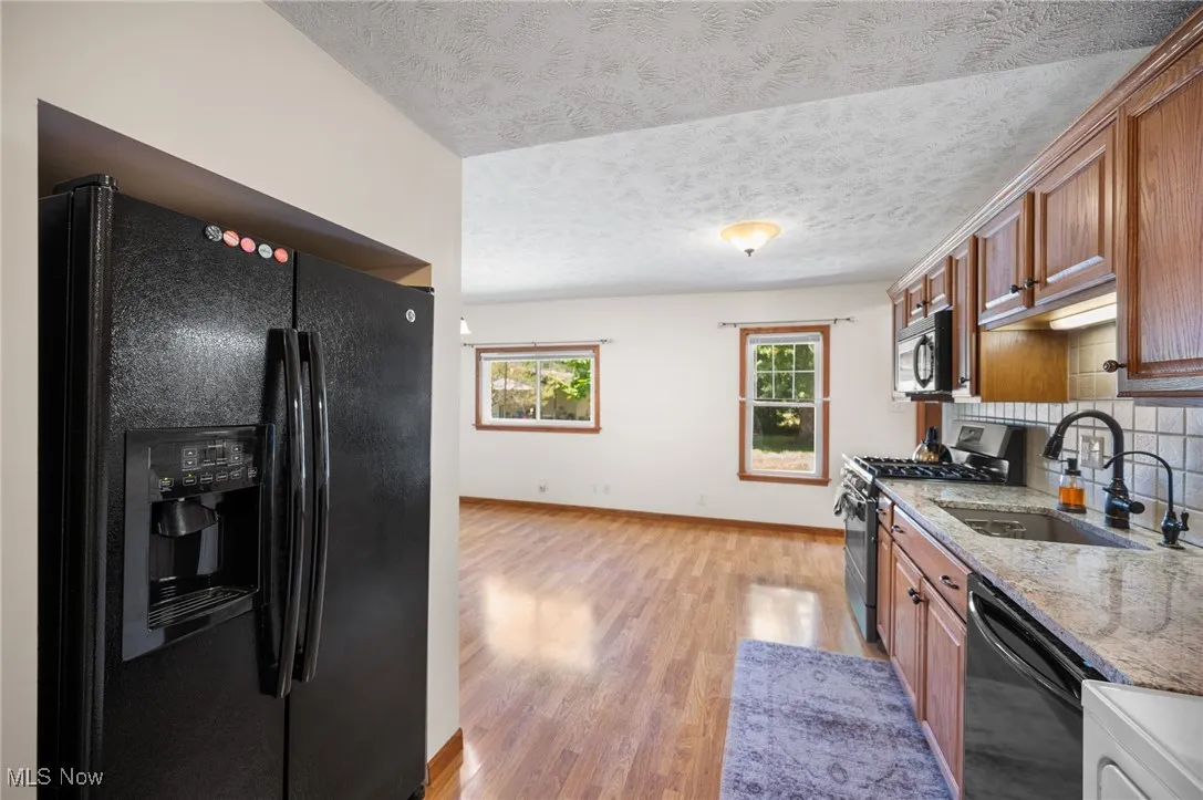 Kitchen featuring black appliances, a textured ceiling, brown cabinetry, light stone counters, and light wood-style flooring