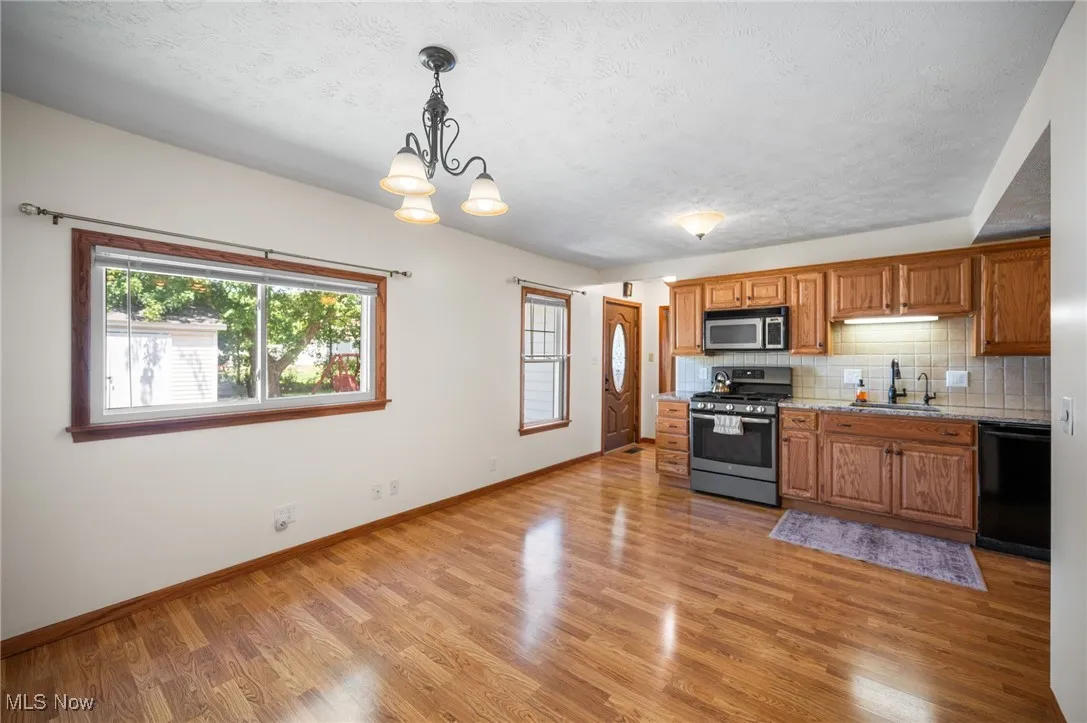 Kitchen with decorative backsplash, appliances with stainless steel finishes, a chandelier, light wood-style floors, and brown cabinetry