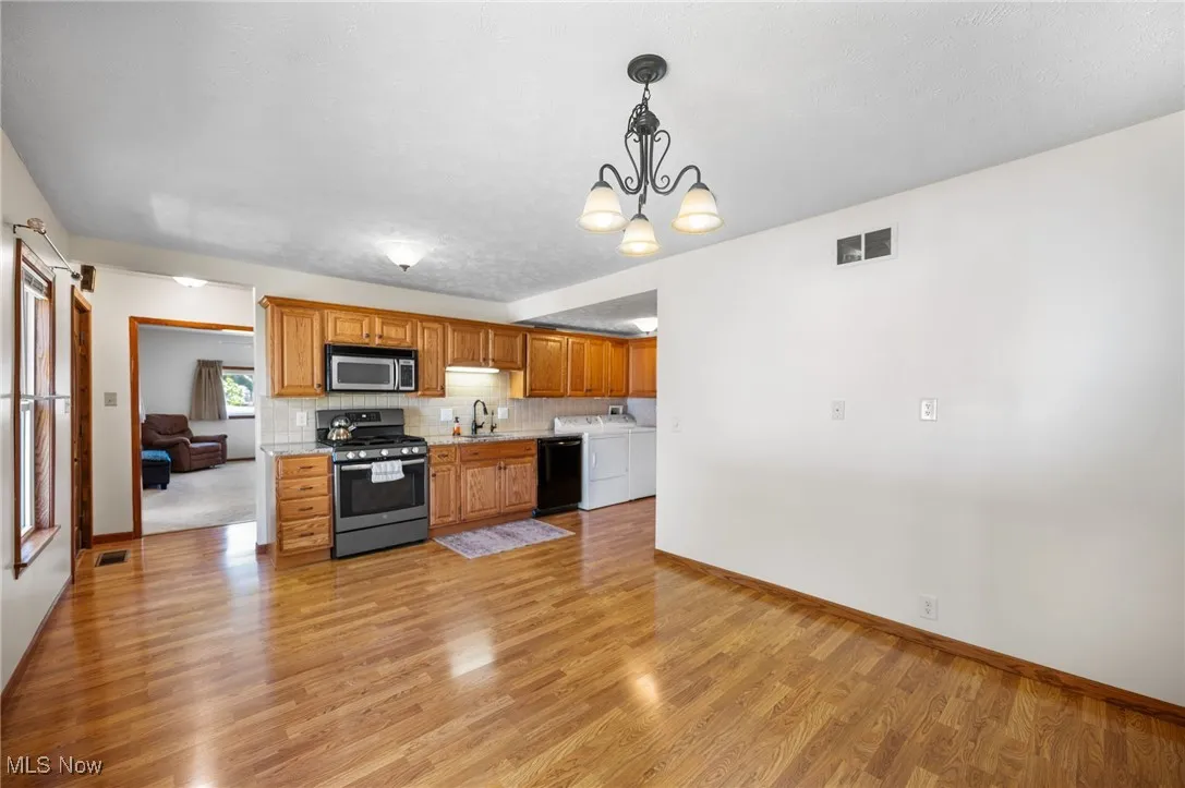Kitchen with washing machine and clothes dryer, appliances with stainless steel finishes, light countertops, decorative backsplash, and brown cabinetry
