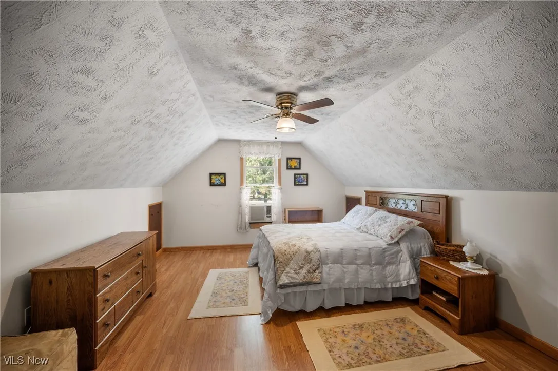 Bedroom with light wood-type flooring, a textured ceiling, lofted ceiling, and ceiling fan