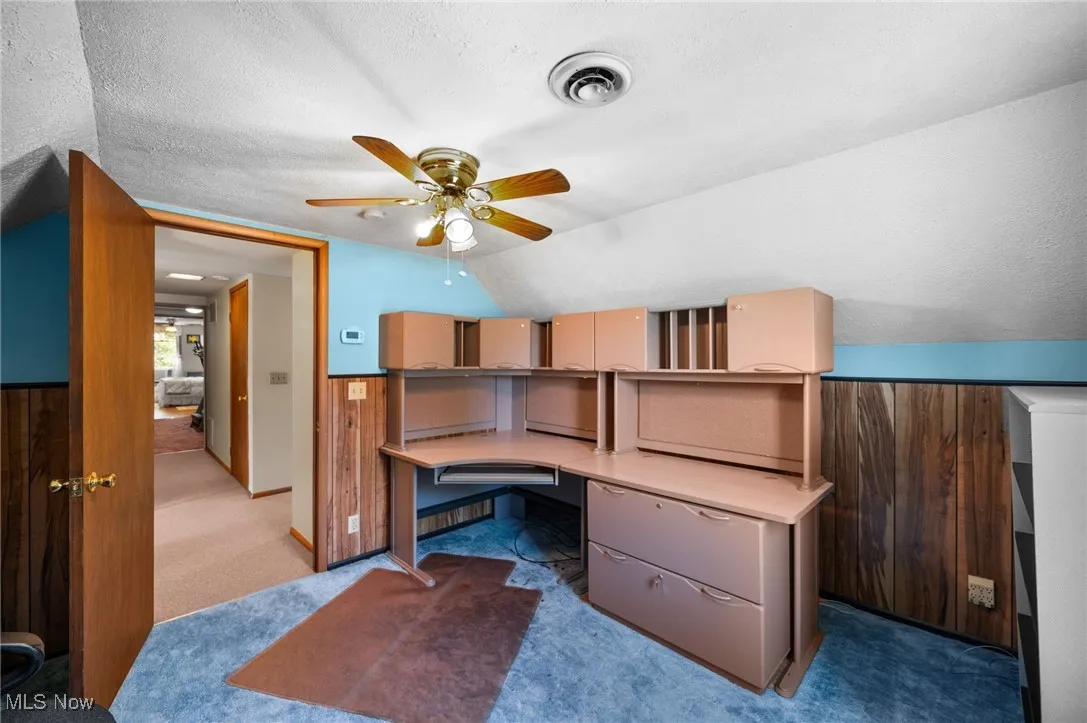 Unfurnished office featuring built in study area, light carpet, a textured ceiling, a ceiling fan, and lofted ceiling