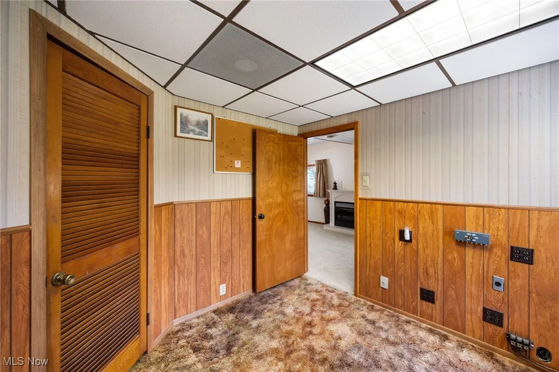 Carpeted empty room featuring a wainscoted wall, wood walls, a paneled ceiling, and wallpapered walls