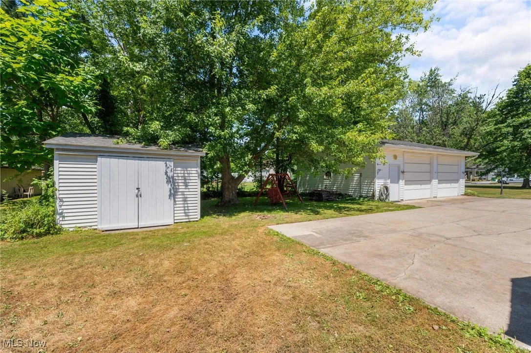 View of green lawn with a detached garage and a shed