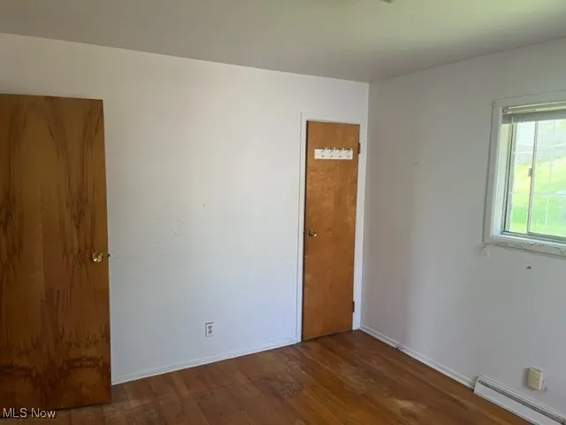Unfurnished room featuring a baseboard heating unit and wood finished floors